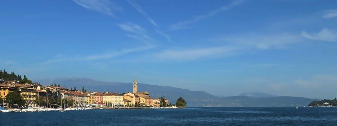 Trip Fit und Aktiv beliebte Urlaubsziele am Gardasee -  Mit einer Fläche von 370 km² ist der Gardasee der größte See Italiens. Es liegt am Fuße der Alpen und erstreckt sich über drei Staaten: Lombardei, Venetien und Trentino. Die maximale Tiefe des Sees beträgt 346 m, er hat eine längliche Form und sein nördliches Ende ist sehr schmal. Dort ist der See von den Bergen der Gruppo di Baldo umgeben. Du trittst aus deinem gemütlichen Hotelzimmer und es begrüßt dich die warme italienische Sonne. Du blickst auf den atemberaubenden Gardasee, der in zahlreichen Blautönen schimmert - von tiefem Dunkelblau bis zu funkelndem Türkis. Majestätische Berge umgeben dich, während die Brise sanft deine Haut streichelt und der Duft von blühenden Zitronenbäumen deine Nase kitzelt. Du schlenderst die malerischen, engen Gassen entlang, vorbei an farbenfrohen, blumengeschmückten Häusern. Vereinzelt unterbricht das fröhliche Lachen der Einheimischen die friedvolle Stille. Du fühlst dich wie in einem Traum, der nicht enden will. Jeder Schritt führt dich zu neuen Entdeckungen und Abenteuern. Du probierst die köstliche italienische Küche mit ihren frischen Zutaten und verführerischen Aromen. Die Sonne geht langsam unter und taucht den Himmel in ein leuchtendes Orange-rot - ein spektakulärer Anblick.